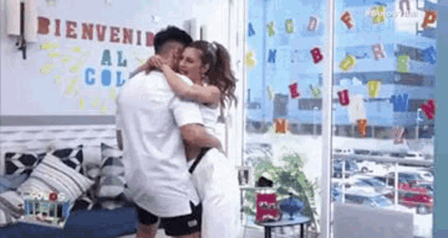 a man and a woman are hugging in front of a sign that says bienvenida .