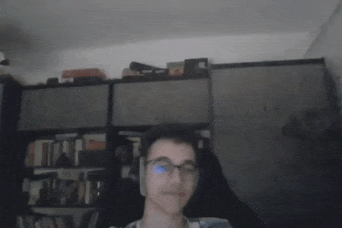 a blurry picture of a man wearing glasses and headphones in front of a bookshelf