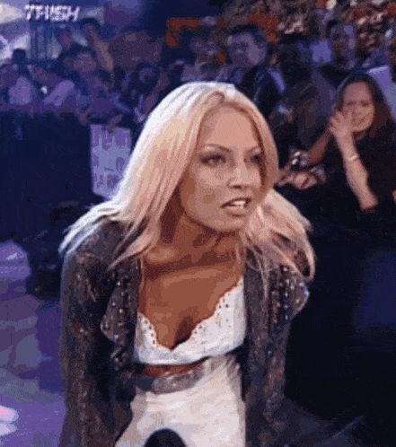 a woman is standing in front of a crowd wearing a leather jacket and a white top .