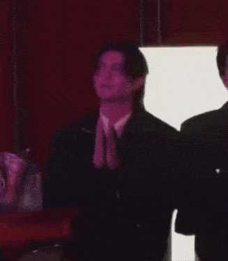 a man in a suit is clapping his hands while standing next to another man .