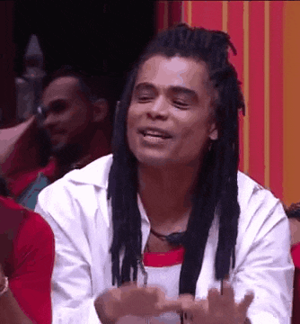 a man with dreadlocks is sitting in front of a group of people and making a funny face .