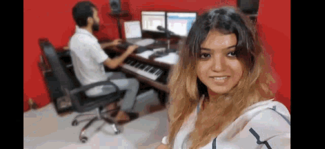 a woman is taking a selfie in a music studio while a man is sitting at a desk .