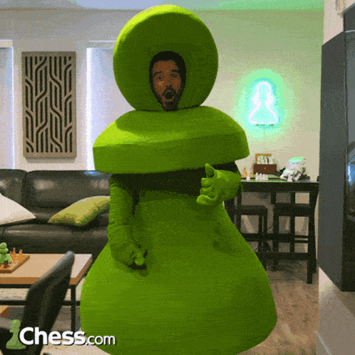 a man in a green chess costume is standing in front of a chess.com logo