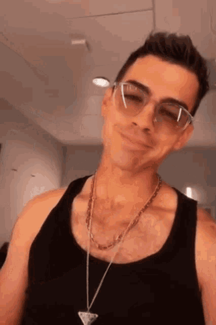 a man wearing sunglasses and a tank top smiles for the camera