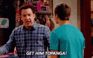 a man in a plaid shirt is talking to another man in a blue shirt who is saying `` get him topanga '' .