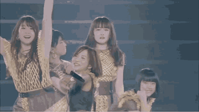 a woman in a gold dress is holding a microphone while dancing on a stage with other women .