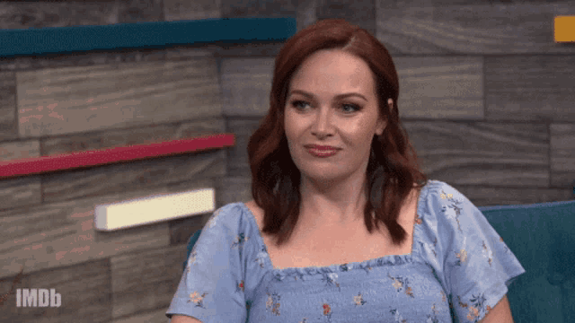 a woman with red hair is sitting on a blue couch with imdb written on the bottom