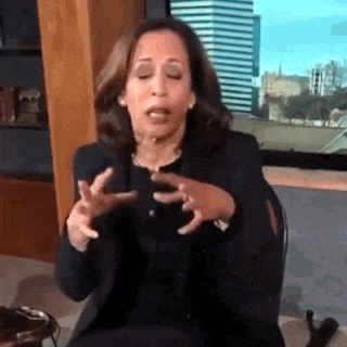a woman in a black suit is sitting in a chair and making a funny face with her hands .