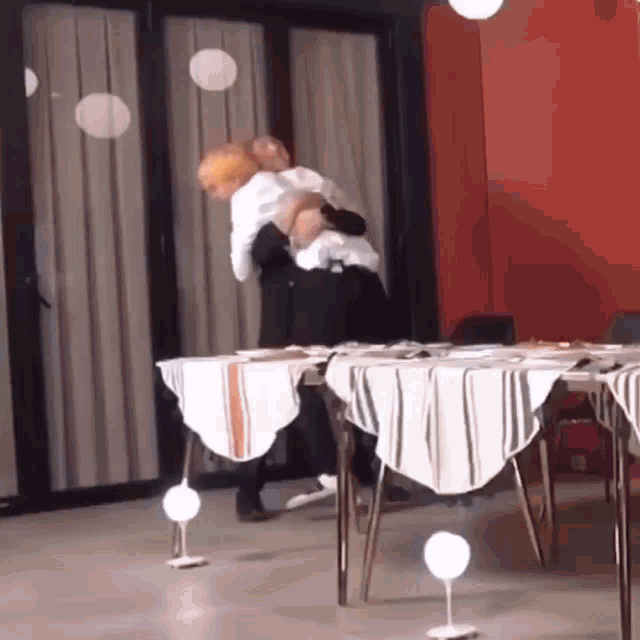 a couple of people are hugging in a room with tables and chairs