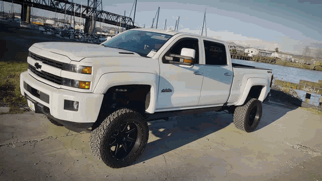 a white truck is parked in front of a body of water and a bridge