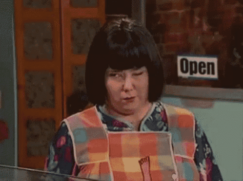 a woman wearing an apron and a wig is standing in front of a sign that says open .