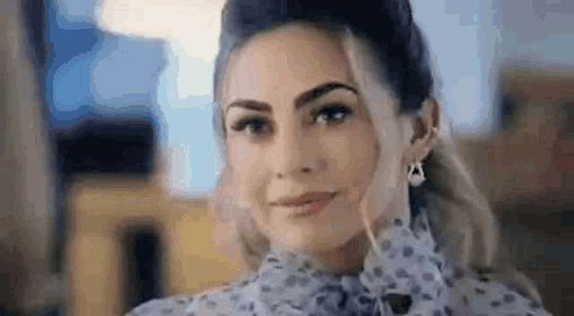 a woman wearing a polka dot shirt and earrings is smiling .