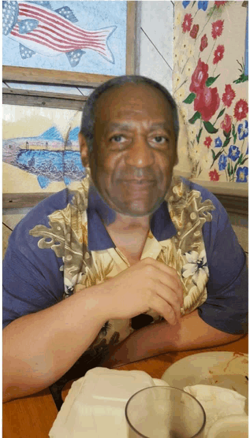 a man in a hawaiian shirt sits at a table with a glass in front of him