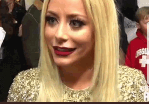 a woman with blonde hair and red lipstick is wearing a gold dress and a red lifeguard shirt .