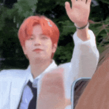 a man with red hair and a white shirt and tie is waving .