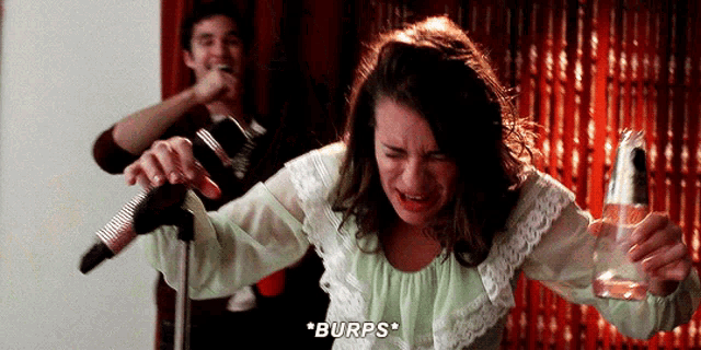 a woman singing into a microphone while holding a bottle of beer and burps