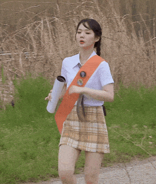 a girl in a white shirt and plaid skirt is running on a road