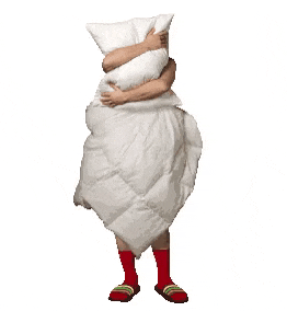 a person wrapped in a white blanket is holding a pillow in front of their face .