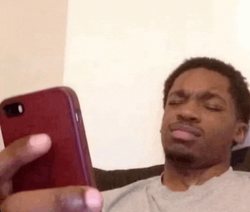 a man is making a funny face while looking at his cell phone .