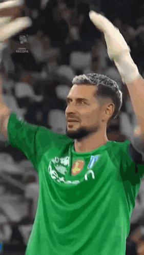 a soccer player wearing a green shirt and white gloves is raising his hands in the air .