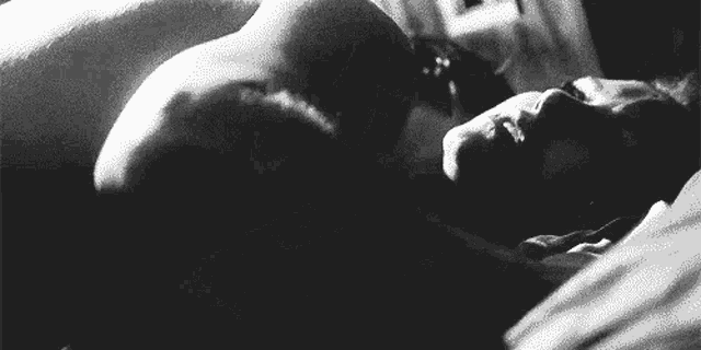 a black and white photo of a man laying on top of a woman on a bed .