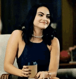 a woman in a black tank top is sitting in a chair holding a cup of coffee and smiling .