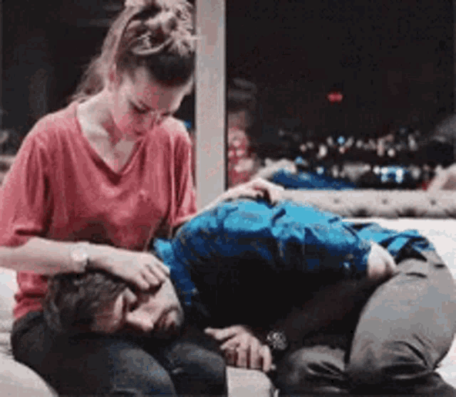 a woman is putting her hand on a man 's forehead while he sleeps on a bed .