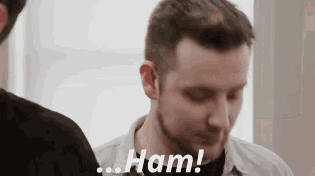 a man with a beard is standing next to another man and says `` ham '' .