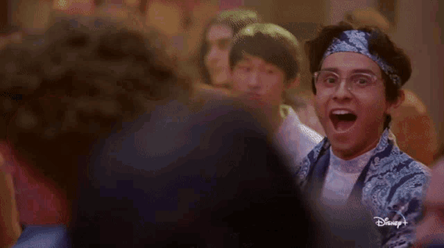 a man with glasses and a bandana on his head is standing in front of a crowd of people .
