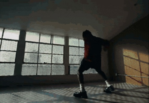 a man in a black hoodie is standing in a room with lots of windows