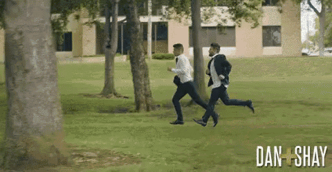 two men in suits are running in a park and the words dan and shay are visible