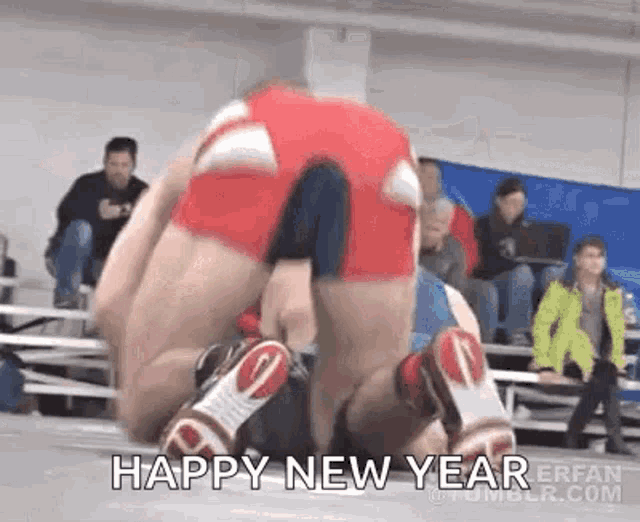 a wrestler is laying on top of another wrestler in a wrestling match while a crowd watches .