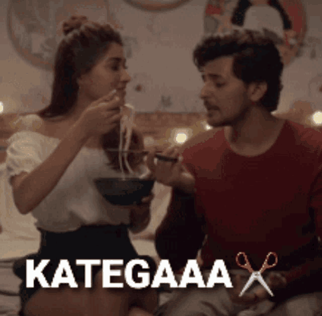 a woman is feeding a man a bowl of noodles and the word kategaaa is on the bottom of the image