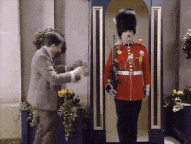 a man in a suit stands next to a man in a red uniform with flowers on it