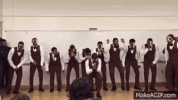 a group of men in tuxedos and bow ties are dancing in a classroom .