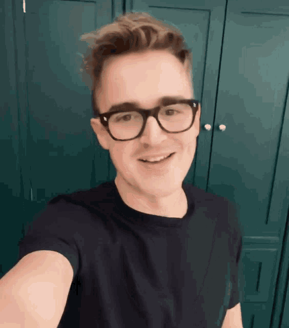 a man wearing glasses and a black shirt is smiling for the camera