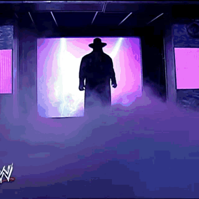 a silhouette of a man in a hat is standing in front of a purple wall
