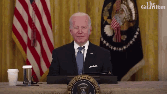 the president of the united states is sitting at a table with the seal of the president of the united states