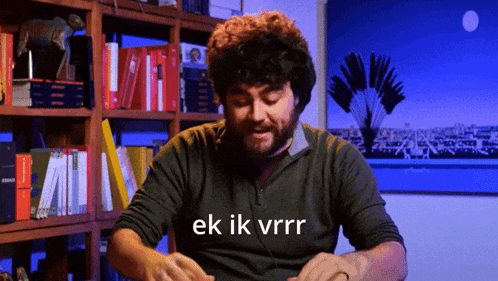 a man with a beard says ek ik vrrr in front of a bookshelf full of books
