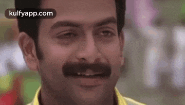 a close up of a man with a mustache and a yellow shirt .