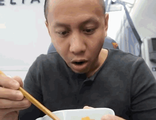 a man is eating something with chopsticks in front of a wall with the word delta on it