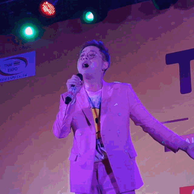 a man in a purple suit sings into a microphone at the thai expo