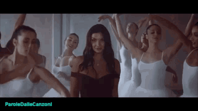 a woman is standing in front of a group of ballerinas in white dresses .