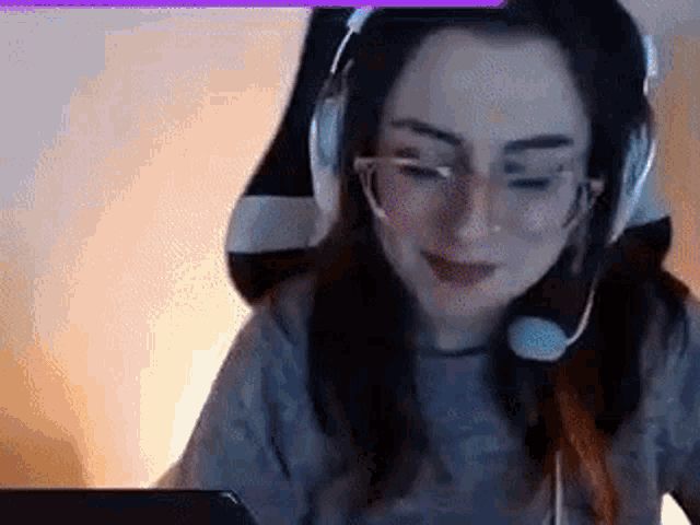 a woman wearing headphones and glasses is sitting in front of a computer screen .