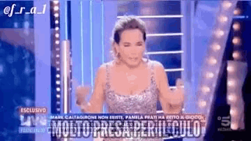 a woman in a silver dress is standing on a stage with her arms outstretched while talking on a television show .