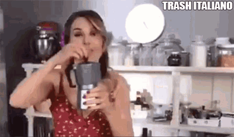 a woman is drinking from a blender in a kitchen and the words trash italiano are above her .