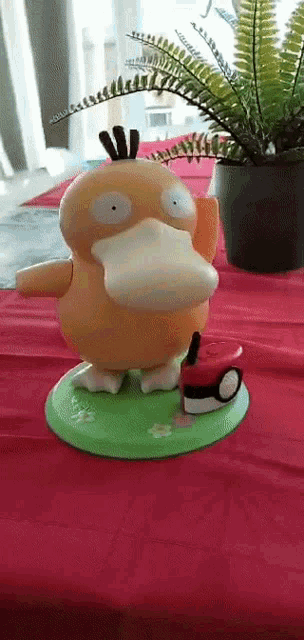 a toy duck is standing on a table next to a plant