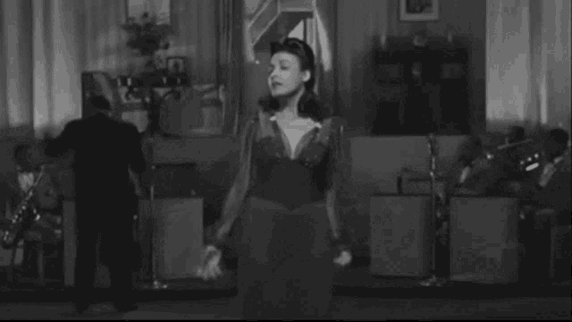 a black and white photo of a woman singing with a band behind her
