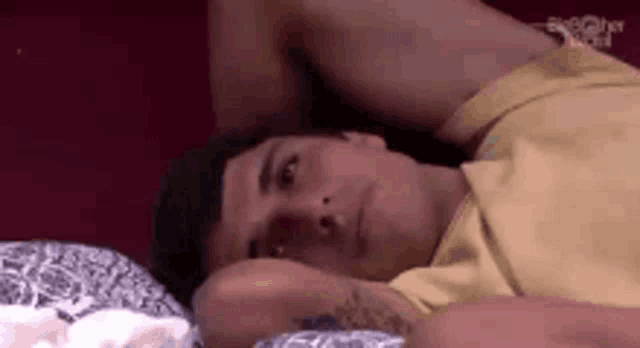 a man in a yellow shirt is laying on a bed with his arms over his head .