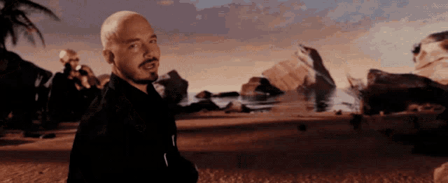 a bald man with a beard is standing in a desert scene